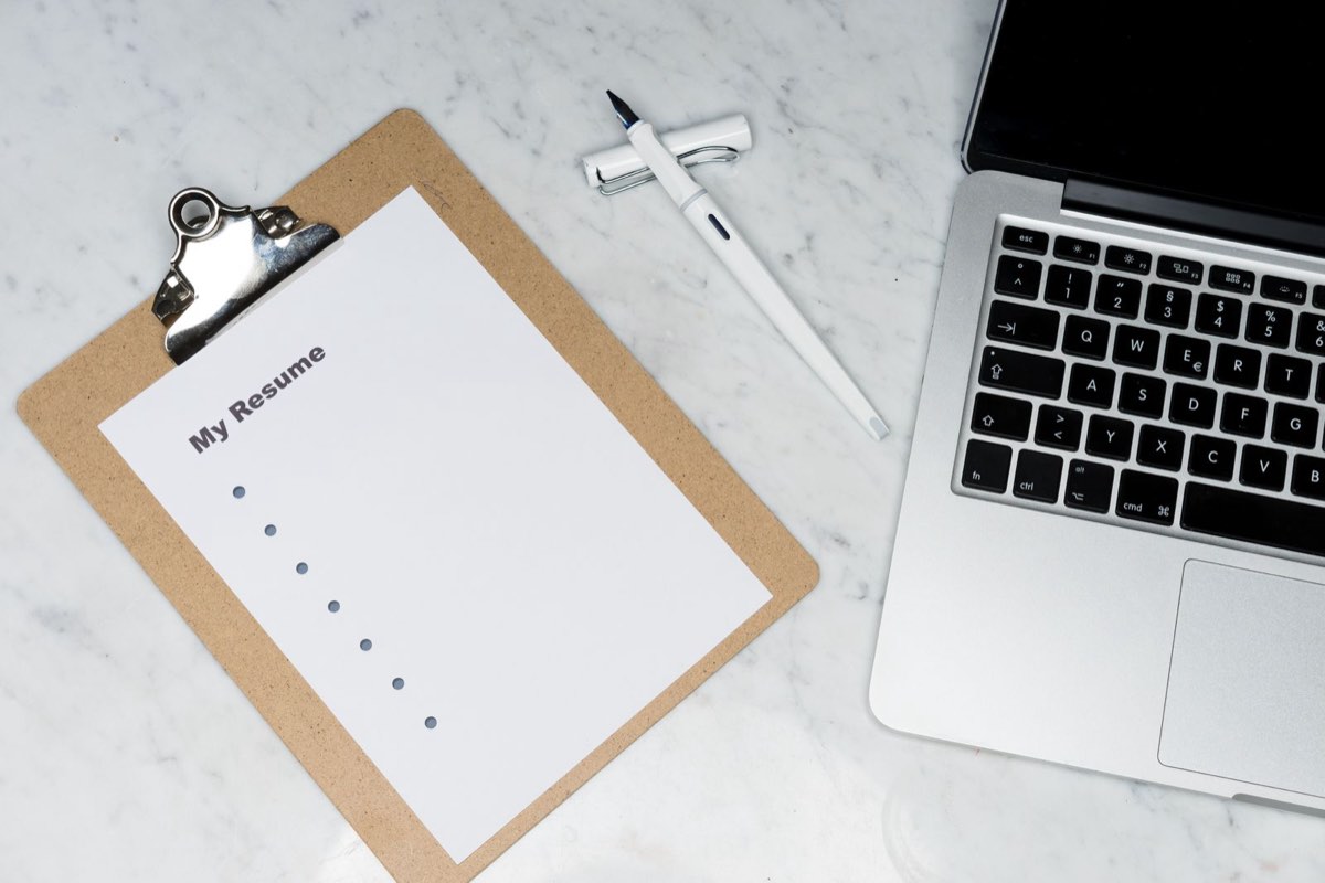 Job seeker editing a resume on a laptop with a notepad and coffee on the desk