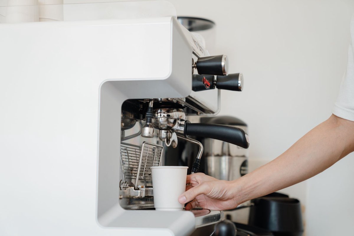 Barista placing a paper cup under an espresso machine group head to pull a shot