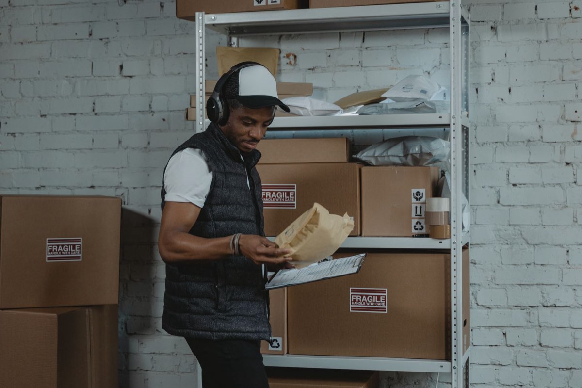 Package handler checking parcels and paperwork next to shelves of boxes in a sorting area
