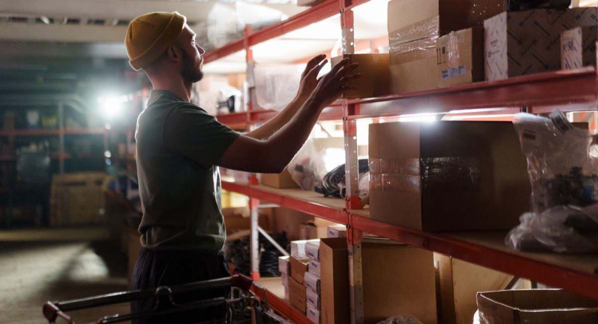 Stocker reaching for a box on a warehouse shelf during a night shift while restocking inventory