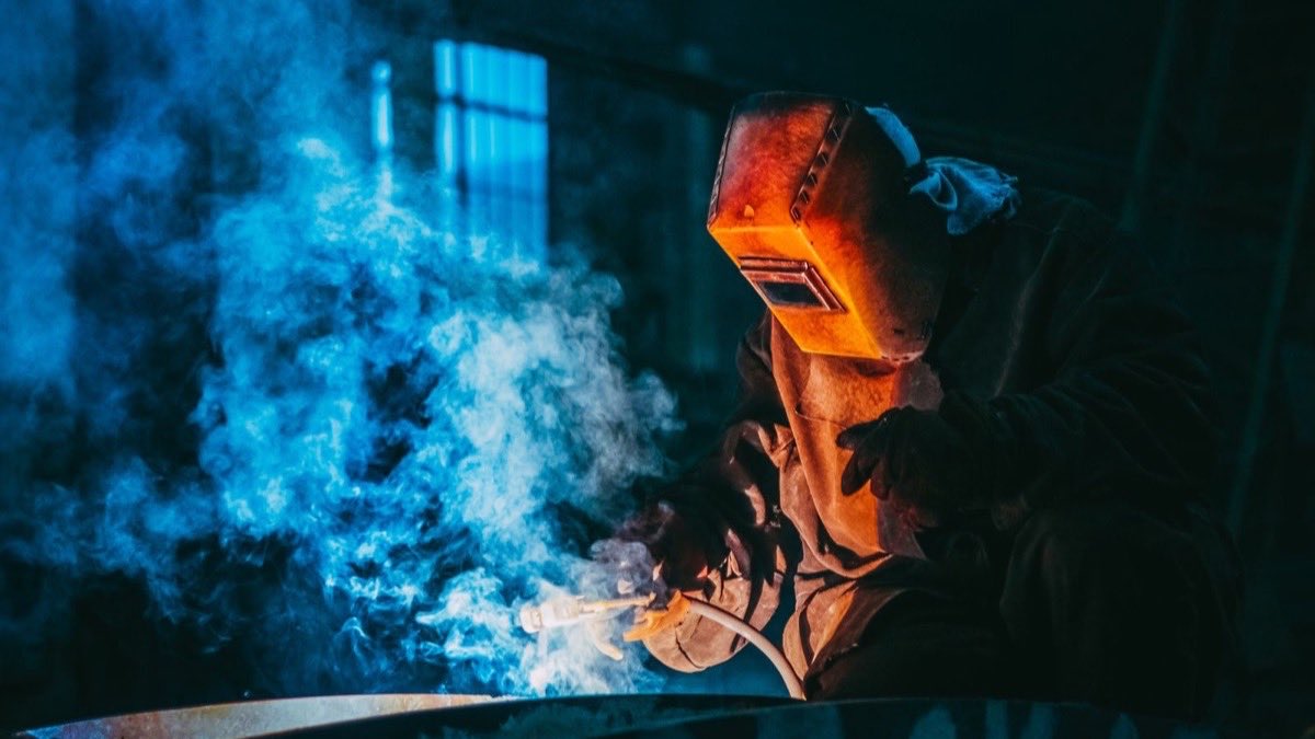 Welder in a helmet and protective gear MIG welding a steel joint with sparks flying